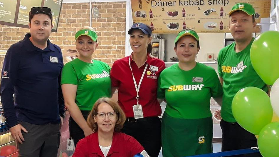CampBondsteel General Manager Lori Maggard, kneeling, poses with local residents who work for the Exchange's new Subway at Kosovo's Camp Bondsteel.