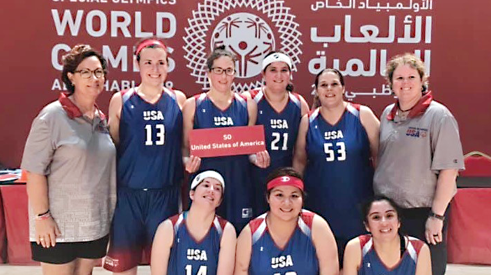 US Women's BBall Fort Sam Houston Associate Jamie Holt, holding sign, joins her teammates at the Special Olympics World Games.