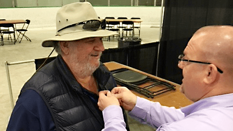 Legion10 Exchange General Manager Brian Read pins a Vietnam Veteran lapel pin on the coat of a Veteran.