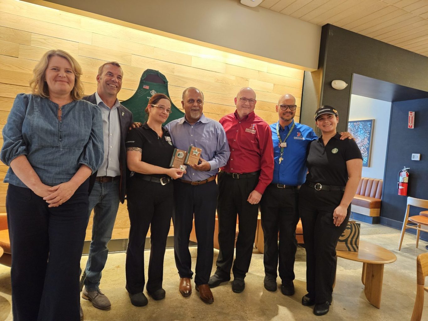 Fort Liberty_Starbucks Award TK Karolyn Madera 2024 <b>Starbucks leaders honor Fort Liberty Exchange leaders for their contributions to the success of the Starbucks location. From left: Regional Director Starbucks Sarah Zabrosky; Starbucks License District Manager Ted Brown; Exchange Facility Manager North Post Starbucks Karolyn Madera; Exchange General Manager Thomas "TK" Kuttamperoor; Regional Vice President, Central Eastern Chris Holifield; Mini Mall Starbucks Store Manager Caroll Poston; and Fort Liberty South Post Starbucks Store manager Francelis Fuster. </b>