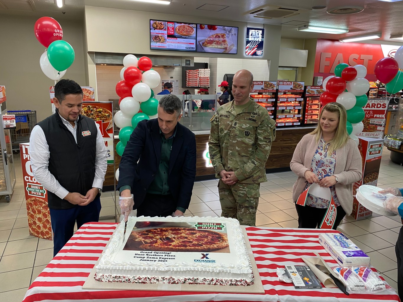 Four people cutting a cake at the Zama Express Hunt Brothers Pizza grand opening.