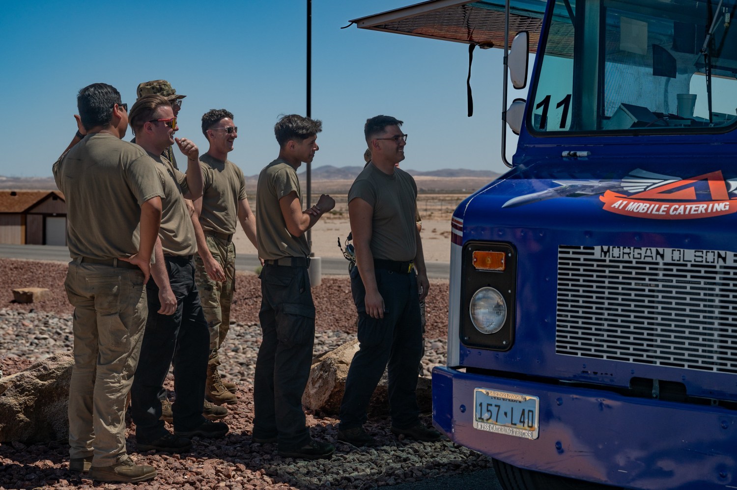 U.S. Airmen line up to order lunch from a food truck in the munitions area at Nellis Air Force Base (AFB), Nevada, May 21, 2025. Historically, operations east of the flightline at Nellis AFB lacked nearby dining options, and the approval of food trucks now provides Airmen with convenient access to meals without requiring them to leave their work zones. (U.S. Air Force photo by Airman 1st Class Jennifer Nesbitt)