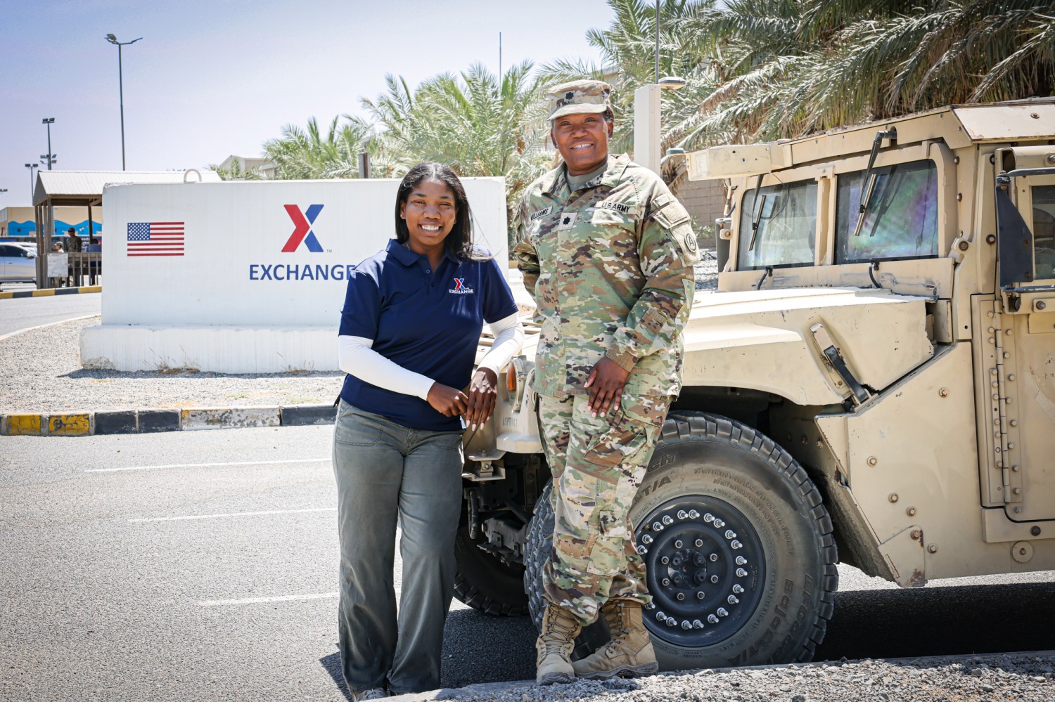 Photo of Colette Watson and Army Lt. Col Regina Williams leaning on a military vehicle in Kuwait. Exchange sign with American flag in background.