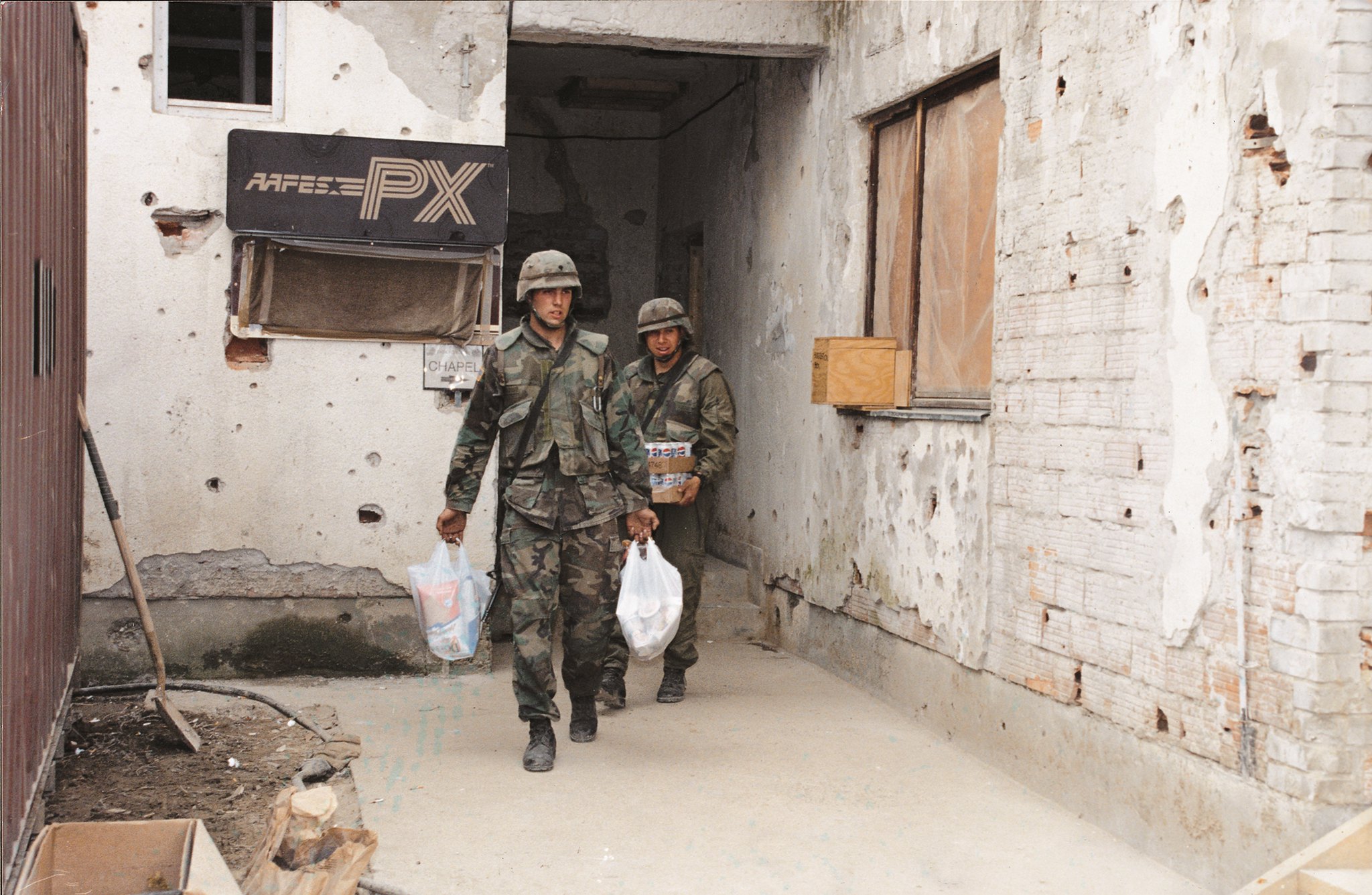 Two Soldiers Carrying AAFES bags while leaving PX in austere brick building