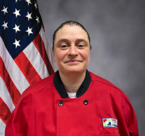 Photo of Anne Marie Johnson, standing in front of American flag and wearing red shirt with Exchange School Meal Program patch.