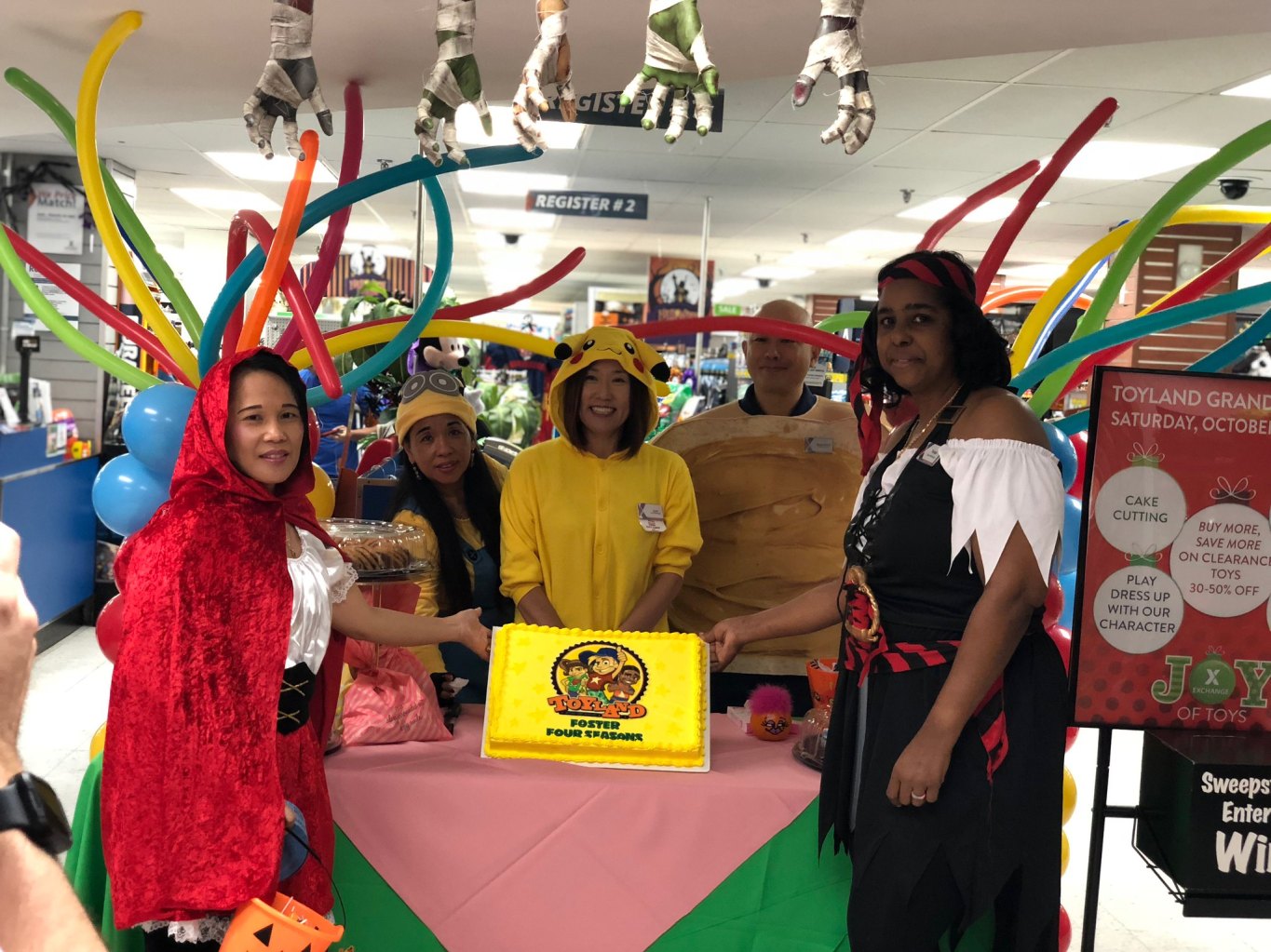 2018 photo of Camp Foster associates in Halloween costume, opening Toyland. Five skeleton hands hang from top of photo.