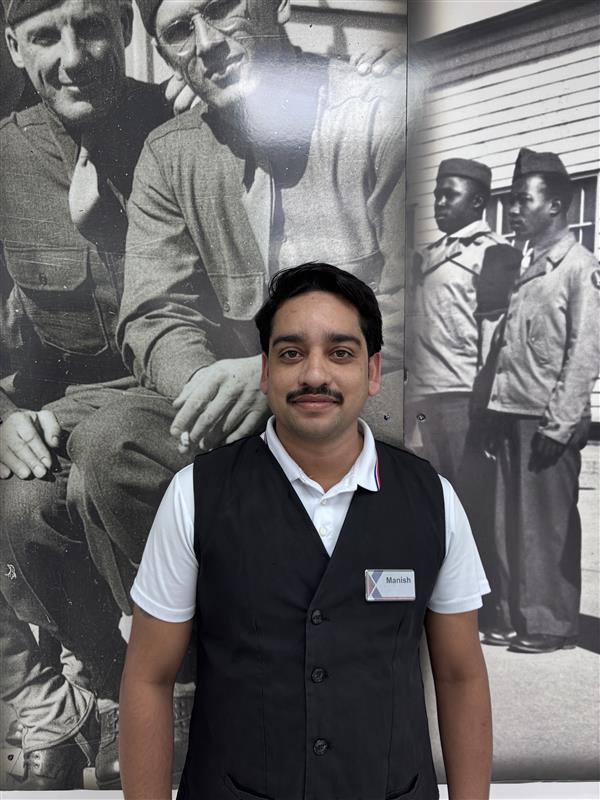 Photo of Mr. Manish, wearing Exchange badge and standing in front of large historic black and white photos.