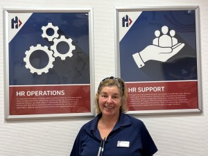 Photo of Silvana Querinuzzi, wearing Exchange shirt and badge, standing in front of HR posters.