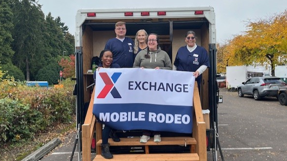 Five Exchange associates at the back of a truck, holding "Exchange Mobile Rodeo" banner.
