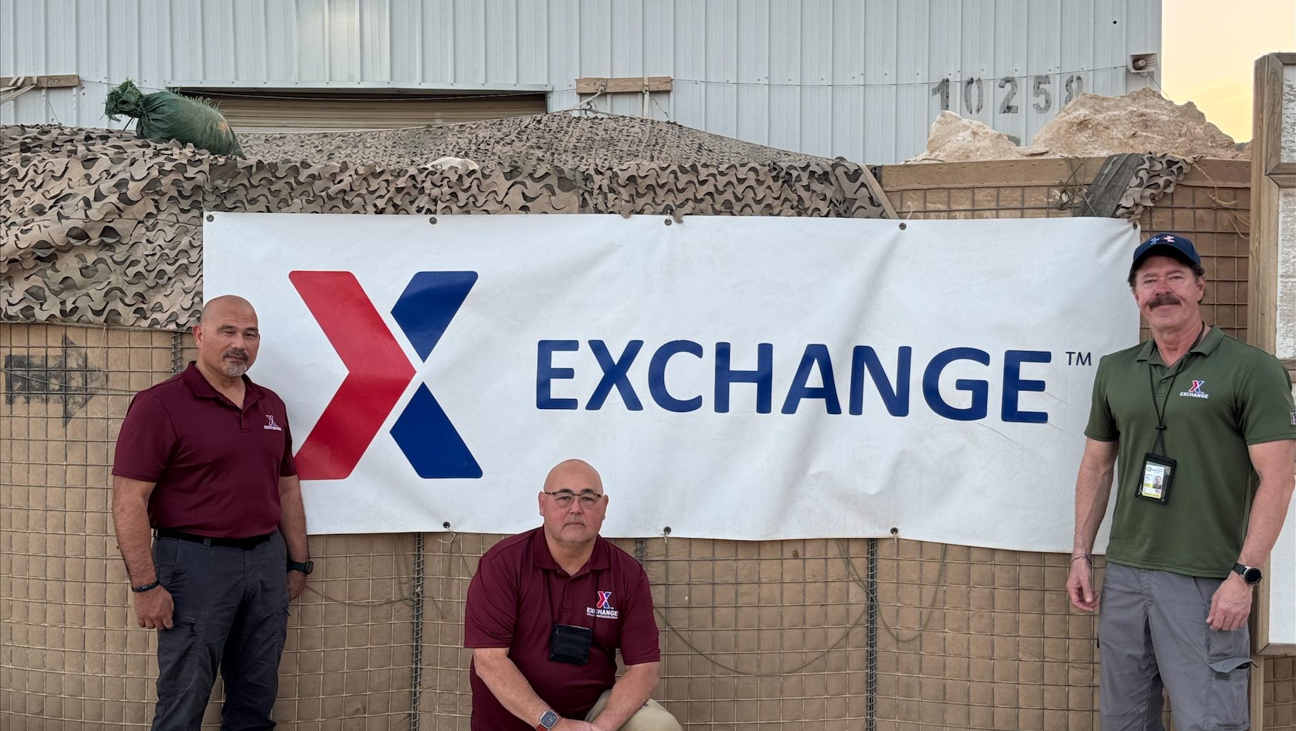 Three men in front of an Exchange banner in Iraq.