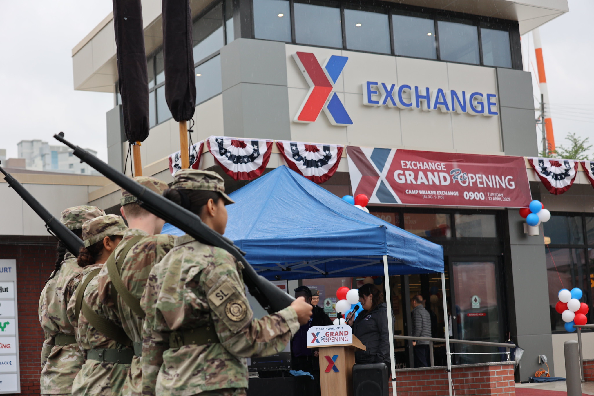 Military honor guard at the April grand opening of the renovated Camp Walker Exchange, with building and Exchange logo in background.