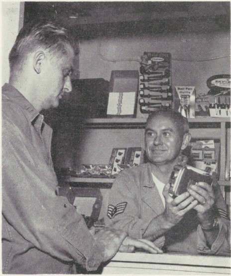 1959 photo of BX manager showing Airman a handheld movie camera.